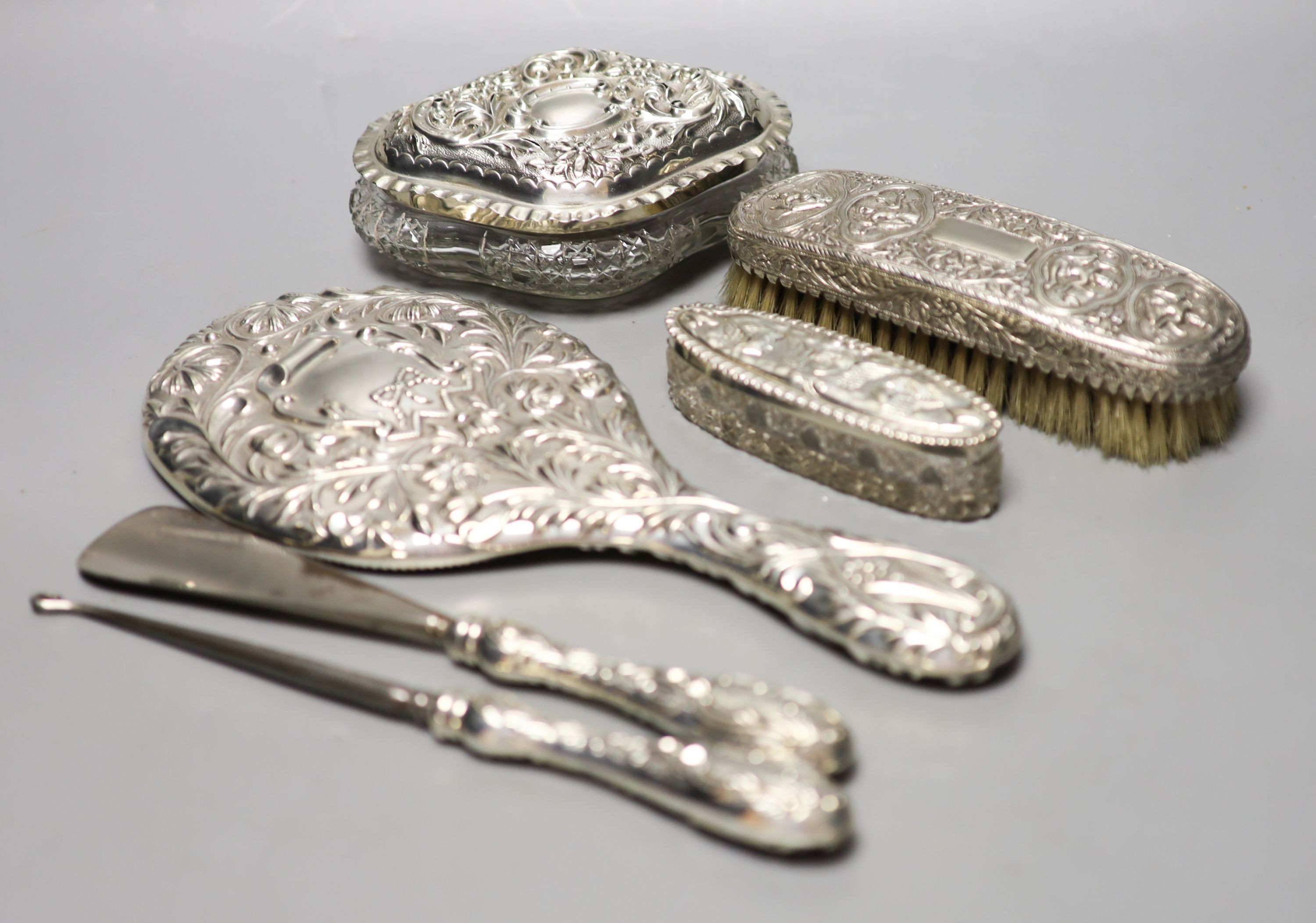 A late Victorian repousse silver mounted hand mirror, London, 1899, two silver mounted glass toilet jars, a silver handled button hook, silver handled shoe horn and a clothes brush.